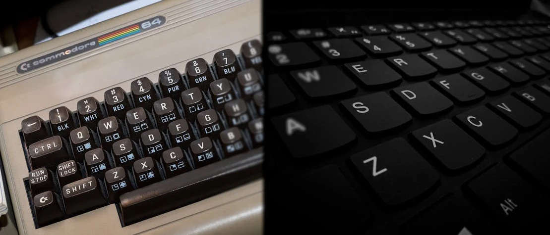 Two keyboards on either side of the screen, one from the Commodore 64 and the other from a modern Mac.